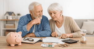 Älteres Ehepaar überprüft gemeinsam Haushaltsunterlagen und Rechnungen am Tisch, mit Sparschwein, Geld und Taschenrechner als Symbol für private Finanzen und Ruhestandsplanung.