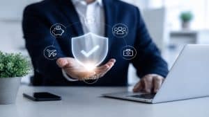 Die Bilddarstellung ergänzt dieses Thema durch eine moderne und minimalistische Szene aus dem Unternehmensumfeld. Ein leuchtendes Schutzsymbol über der Hand eines Geschäftsmannes steht für Sicherheit, digitale Innovation und intelligente Absicherung. Die visuellen Elemente vermitteln eine Verbindung zwischen Technologie, Vertrauen und der Zukunft des deutschen Versicherungsmarktes im Bereich Finanzen und digitaler Transformation.